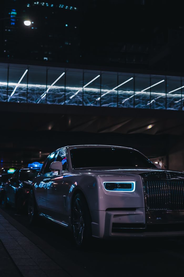 A luxury car parked on a city street at night, illuminated by neon lights. Urban elegance.